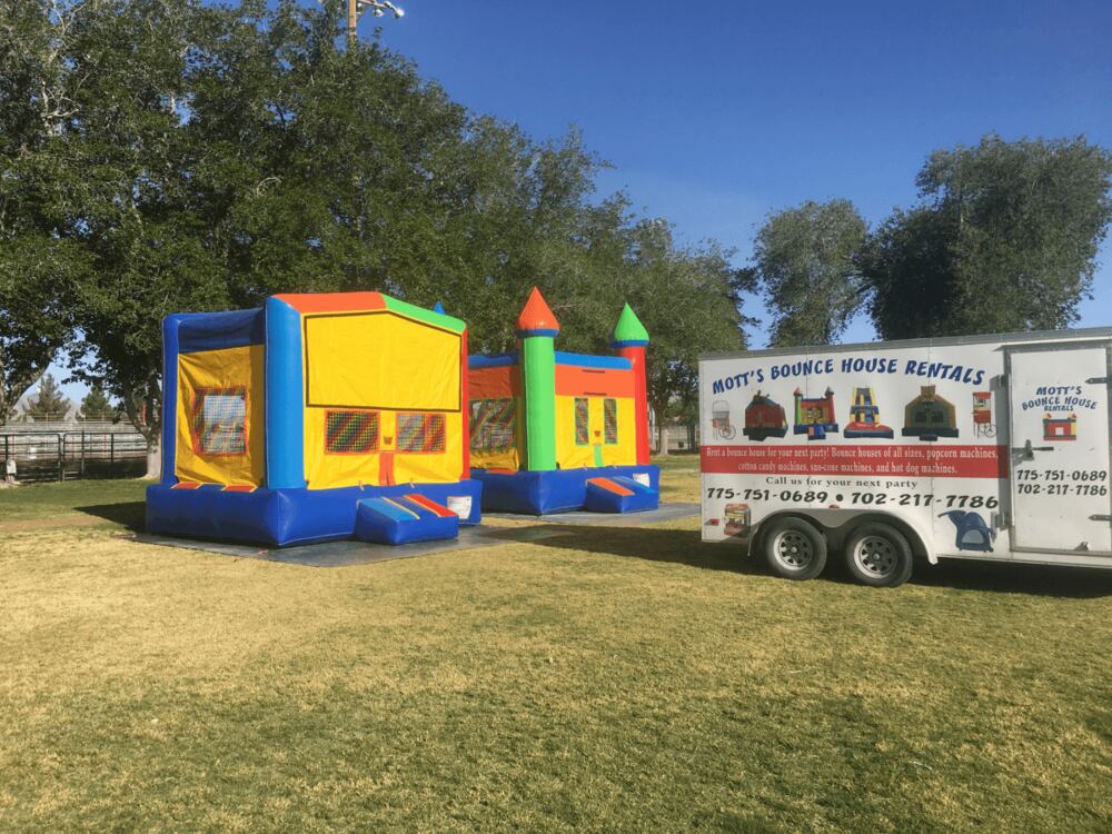 A row of colorful bounce houses and combo units set up on a lawn next to the Mott's trailer